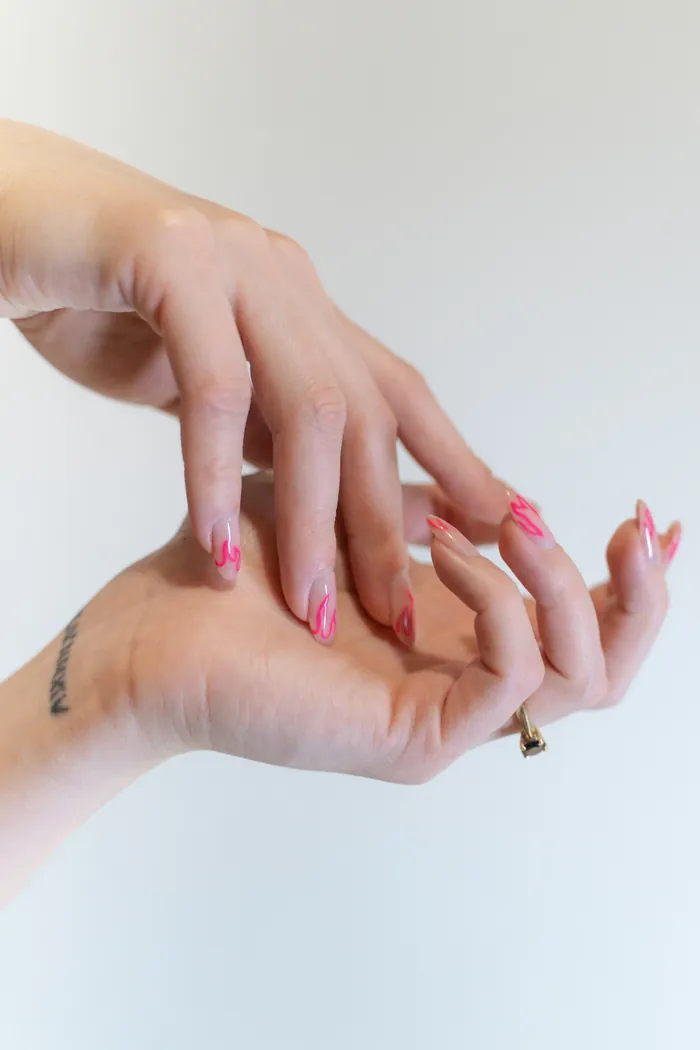 Mãos com unhas rosa e detalhes em branco